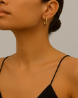 A woman with smooth, medium skin and dark hair in a low bun wears a black spaghetti strap top by Princess Goes Hollywood and chunky vergoldete Creolen. Only her lower face, neck, and part of her shoulder appear against a neutral background.