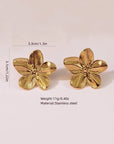 Zwei goldfarbene Edelstahl-Ohrstecker von Princess Goes Hollywood in Form fünfblättriger Blumen (3,3 x 3,1 cm, 11 g) stehen aufrecht vor dezent hellrosa Hintergrund.