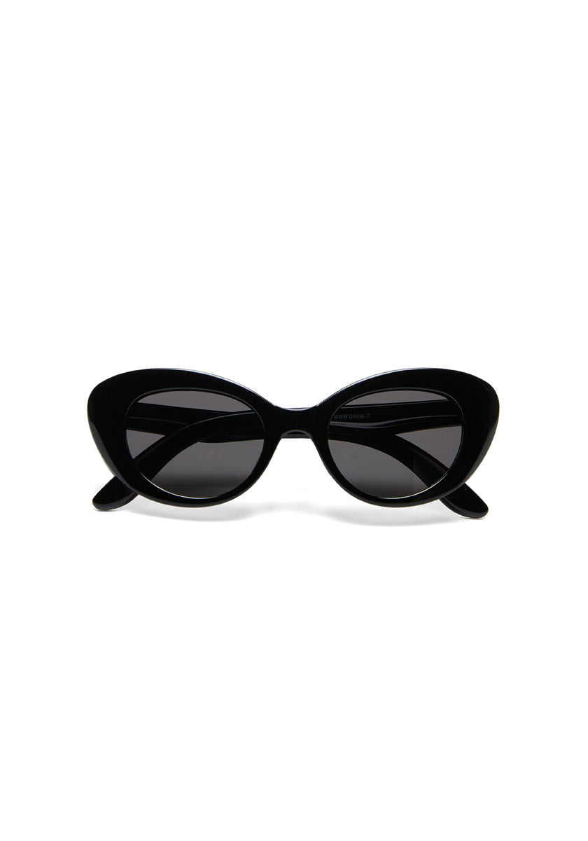 A pair of black cat-eye Parigi sunglasses by Okkia, featuring thick, glossy frames and dark tinted lenses, is displayed facing forward against a plain white background with partially visible outward-angled arms.
