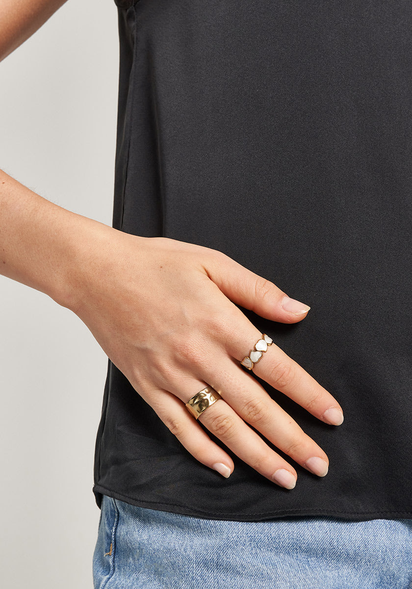 A person in a black shirt and light blue jeans rests their left hand on their hip, showing off neatly trimmed nails and wearing the Ring mit Herzen in Perlmutt-Optik by Princess Goes Hollywood among other rings.