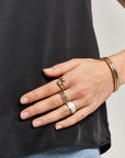 A person in a black top and blue jeans rests their left hand on their hip, showing off bold rings like the Vergoldeter Ring in Tropfenform by Princess Goes Hollywood and a gold bangle, all standing out against their simple outfit.