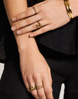 A person with light skin wears the Princess Goes Hollywood Vergoldeter Ring in Tropfenform. Their short natural nails and black outfit highlight their crossed arms for a chic look.