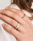 A left hand with neatly trimmed nails wears two rings: a gold open ring on the index finger and Princess Goes Hollywoods Ring mit Herzen in Perlmutt-Optik on the ring finger. The hand rests on white textured fabric.