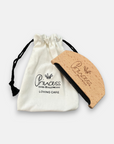 A curved Princess Goes Hollywood Kaschmirkamm aus Buchenholz sits next to a white drawstring pouch with the logo and LOVING CARE print. The set is ideal for gentle detangling and minimizing pilling.