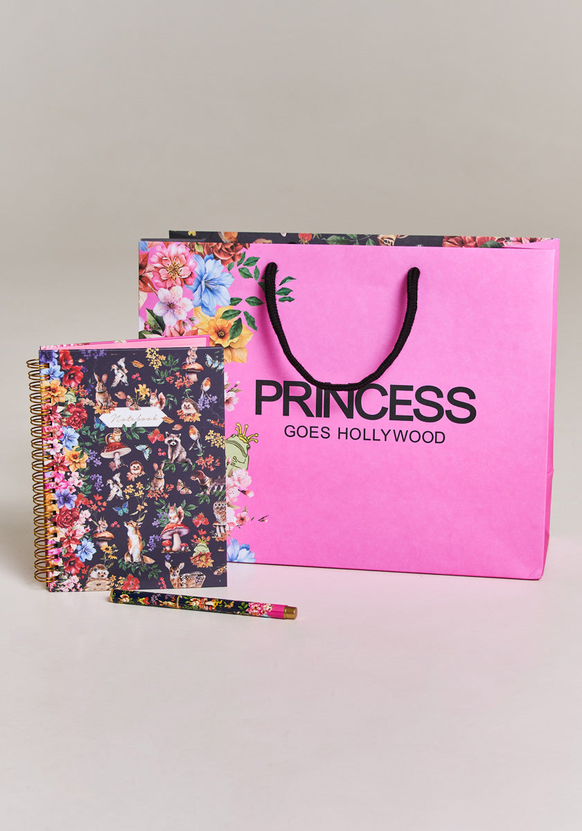 A pink Princess Goes Hollywood gift bag stands behind an A5 Notizbuch Forest Animals with floral and woodland covers, a matching floral pencil, and a smaller book, all neatly arranged on a light grey surface.