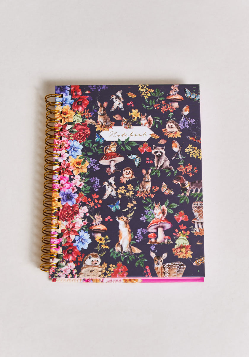 The Notizbuch Forest Animals by Princess Goes Hollywood is an A5 spiral-bound notebook with a dark cover featuring colorful woodland animals and flowers, plus “Notebook” in cursive at the center.