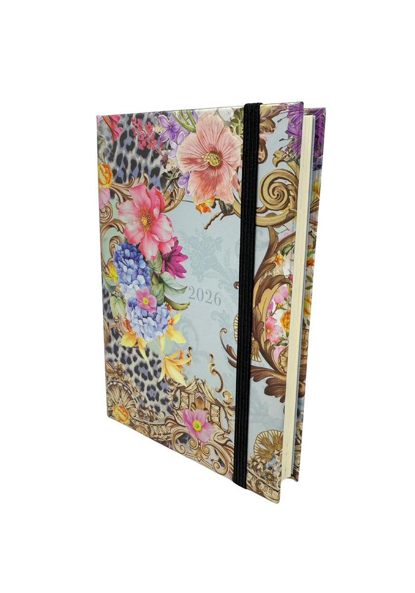 A hardcover Jahresplaner 2026 by Princess Goes Hollywood with a decorative cover of colorful flowers, gold scrolls, and leopard print accents. Features a black elastic closure and stands upright to show cream-colored pages.