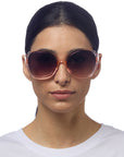 A woman with straight dark hair pulled back wears Okkia oversized round butterfly-style sunglasses with UV protection and a translucent frame. She has a neutral expression and is dressed in a plain white top against a white background.