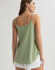 A woman with long brown hair faces away, wearing a light green Bella Dahl Lyocell top with adjustable straps and frayed edges, paired with white shorts. Her left hand rests by her side against a neutral background.