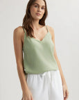 A woman with long brown hair and light skin stands against a plain background wearing a Bella Dahl light green Lyocell Trägertop with frayed edges and loose white drawstring shorts. She has a neutral expression and one hand by her side.