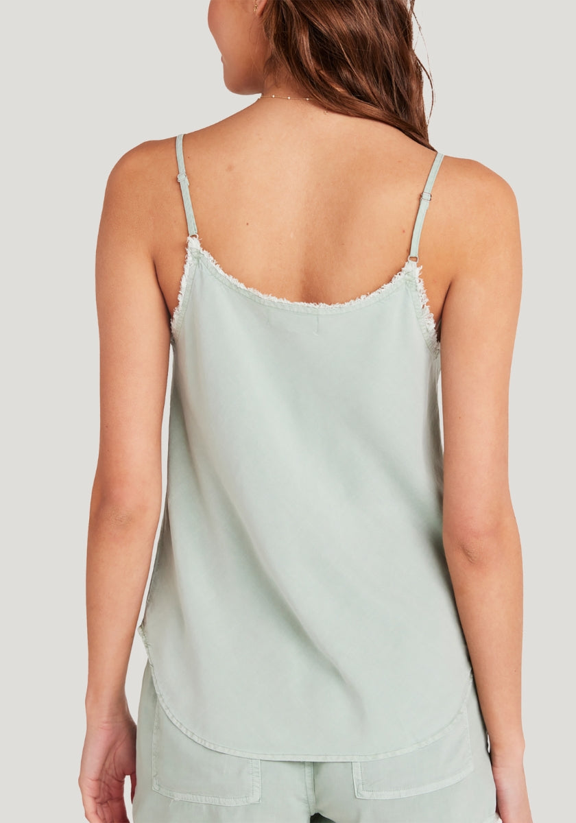 A woman with long brown hair wears a light sage green Bella Dahl Lyocell Trägertop with thin, adjustable straps and frayed edges, paired with matching shorts. She is shown from the back against a plain light background.