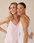 Two women stand close, smiling. One wears a light pink Bella Dahl Trägertop with frayed edges in denim look and has wavy blonde hair; the other, a white Bella Dahl Lyocell sleeveless top, with straight dark hair pulled back and hoop earrings.