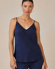 A woman with slicked-back dark hair wears a Bella Dahl navy Lyocell V-neck camisole featuring thin straps and frayed edges, paired with matching pants. She stands facing the camera with a neutral expression against a plain beige background.