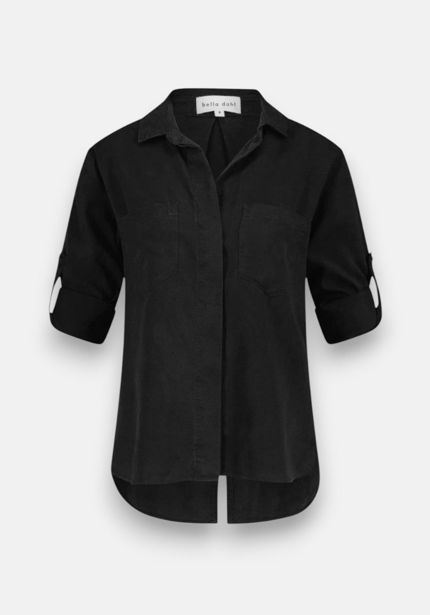 A black Bella Dahl Lyocell button-up blouse with long roll-tab sleeves, collar, two chest pockets, curved high-low hem, and a relaxed fit is shown on a plain white background.