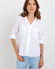 A woman with wavy brown hair wears a sheer white Bella Dahl Lyocell Hemd with rolled sleeves and two chest pockets, paired with light blue jeans. She stands against a plain white background, looking at the camera with a relaxed expression.