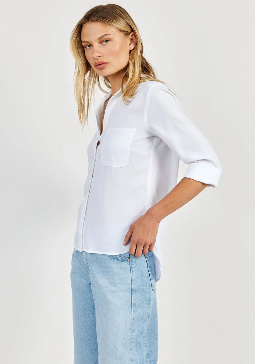 A woman with long blonde hair models an oversized white Hemdbluse by Bella Dahl, crafted from 100% Lyocell, paired with light blue jeans. She poses relaxedly, gazing left against a plain light backdrop.