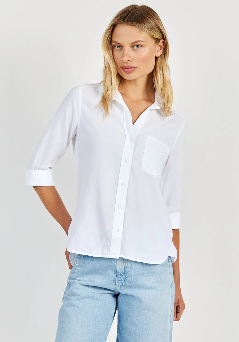 A woman with straight blonde hair models a Bella Dahl 100% Lyocell Hemdbluse in an oversized cut, featuring rolled-up sleeves and chest pocket, styled with light blue jeans. She stands casually against a plain light background.