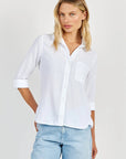 A woman with straight blonde hair models a Bella Dahl 100% Lyocell Hemdbluse in an oversized cut, featuring rolled-up sleeves and chest pocket, styled with light blue jeans. She stands casually against a plain light background.