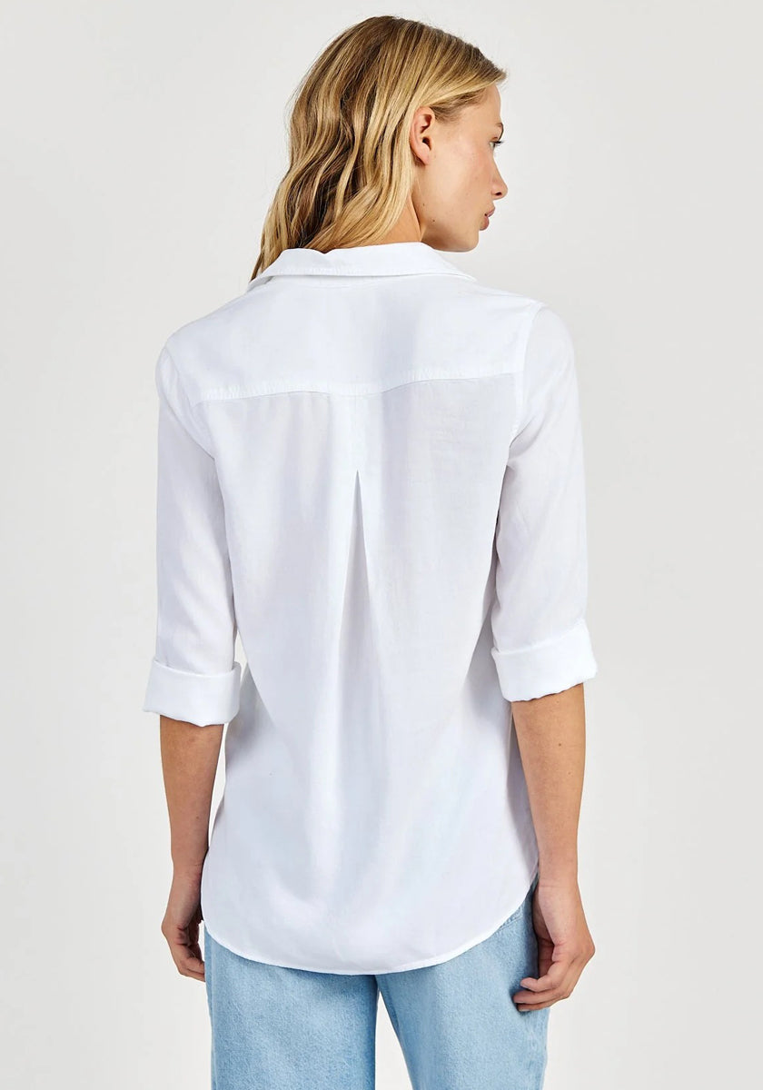 A woman with straight blonde hair faces away, wearing a Bella Dahl oversized Schnitt Hemdbluse in 100% Lyocell with rolled-up sleeves and light blue jeans against a plain, light-colored background.