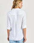 A woman with straight blonde hair faces away, wearing a Bella Dahl oversized Schnitt Hemdbluse in 100% Lyocell with rolled-up sleeves and light blue jeans against a plain, light-colored background.