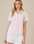 A woman with long blonde hair models a light pink Bella Dahl Lyocell blouse with a Hemdkragen and chest pocket, paired with white shorts. She stands facing forward, lightly smiling against a beige background.