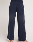 A person stands barefoot on a light background, facing away from the camera, wearing Bella Dahl’s navy blue wide-leg Lyocell pants in denim look with a high smocked waistband and relaxed fit.