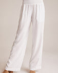 A person wears Bella Dahl’s loose, white wide-leg pants in Denimoptik with a smocked elastic waistband, paired with tan open-toe heeled sandals. The image is cropped from the waist down against a plain light background.