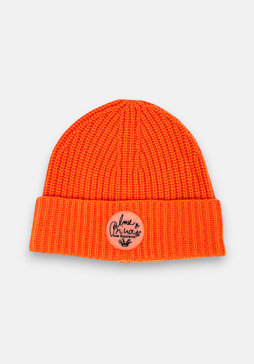 Bright orange knitted beanie by Princess Goes Hollywood with a folded brim and ribbed design, featuring a round beige patch on the front with black handwritten-style text “Palm Oracle” and a small open palm graphic below.
