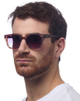 A man with short brown hair and a reddish beard, wearing a white shirt and Okkia unisex square-frame sunglasses with UV 400-Schutz, looks slightly to the side against a plain white background.