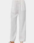 Eine Person trägt eine weite Hose Damen von Bella Dahl mit elastischem Bund und beige Slide-Sandalen mit Cut-out-Details vor weißem Hintergrund. Nur der Unterkörper ist zu sehen – ein lässiger, komfortabler Look.