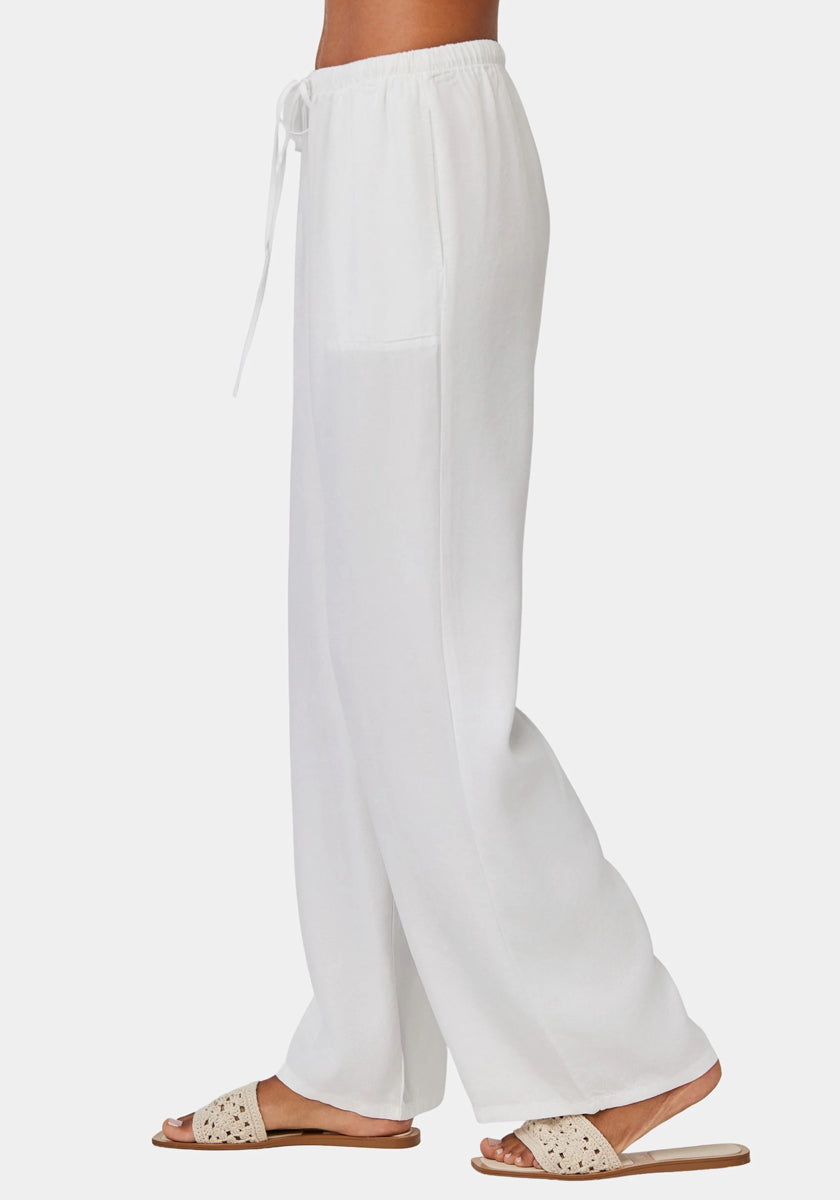 A person is shown from the waist down wearing a loose-fitting Bella Dahl Lyocell womens pant with an elastic waistband and side pockets, plus beige woven slides. The pants have a relaxed fit and slightly sheer fabric against a white background.