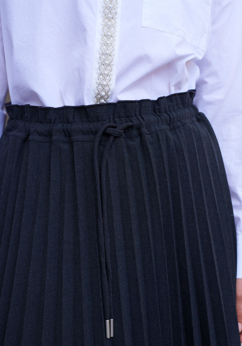A close-up shows a person wearing a white long-sleeve shirt with beaded trim and a high-waisted black pleated skirt with elastic waist and drawstring by Princess Goes Hollywood. The image highlights the midsection details.