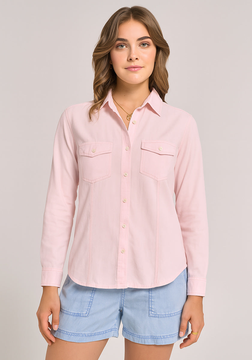 A young woman with wavy, light brown hair wears a light pink Bella Dahl Lyocell Bluse im Jacken-Stil with two breast pockets and light blue denim shorts. She faces forward against a plain, light background, her expression neutral.