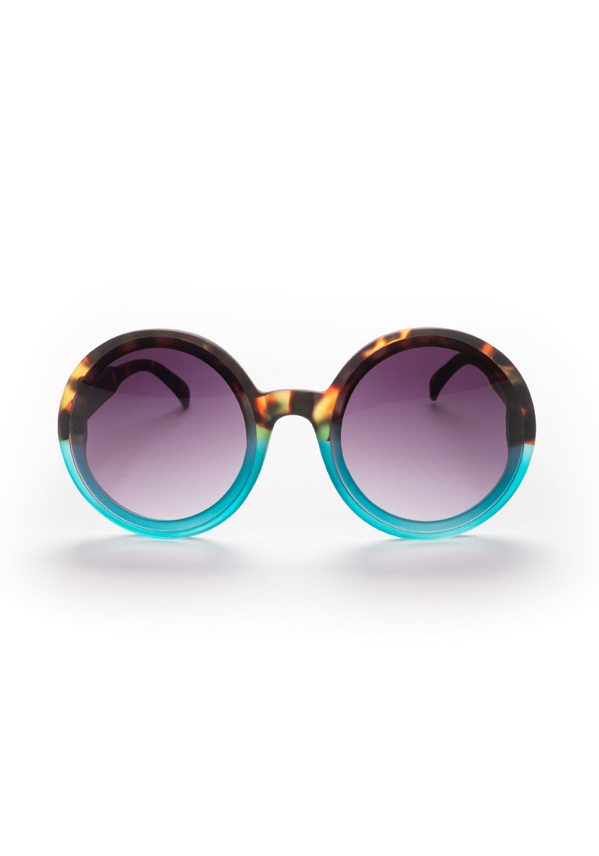 Okkia Round Oversize-Sonnenbrille mit UV 400-Schutz: Große Tortoiseshell-braune und türkisblaue Rahmen, violett getönte Gläser. Perfektes Accessoire für stilbewusste Persönlichkeiten vor weißem Hintergrund.