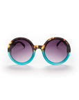 Okkia Round Oversize-Sonnenbrille mit UV 400-Schutz: Große Tortoiseshell-braune und türkisblaue Rahmen, violett getönte Gläser. Perfektes Accessoire für stilbewusste Persönlichkeiten vor weißem Hintergrund.
