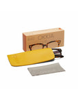 A pair of Okkia tortoiseshell square reading glasses partially in a yellow case, a gray cleaning cloth, and an Okkia branded box with product illustrations—all displayed on a white background.