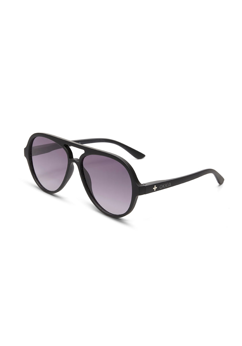 Okkia black-framed sunglasses feature round, dark gradient lenses with UV 400 protection, a keyhole bridge, and sleek unisex temples adorned with a white cross and Okkia text. Displayed angled on a white background.