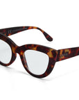 Close-up of Okkia eyeglasses with a bold cat-eye design in brown and amber tortoiseshell. Transparent lenses, with “OKKIA” in white on the left temple arm, set against a plain white background.
