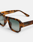Hier ist Ihr überarbeiteter Satz unter Verwendung der bereitgestellten Produktdaten: Nahaufnahme einer Sonnenbrille aus der Okkia CLUB-Kollektion in Schildpattoptik mit rechteckigen grauen Gläsern. Der glänzende, geometrische Rahmen verleiht ihr einen modernen Touch, während der Markenname „Okkia“ in Weiß auf dem linken Bügel zu sehen ist. Der schlichte weiße Hintergrund unterstreicht das schicke Design dieser STROMBOLI-Sonnenbrille.