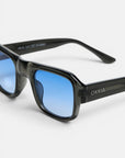 Eine Sonnenbrille mit schwarzem Rahmen und blauen Verlaufsgläsern wird in Nahaufnahme vor einem weißen Hintergrund gezeigt. Auf dem rechten Bügel ist der Markenname „Okkia“ in weißen Buchstaben zu sehen. Diese STROMBOLI-Brille ist Teil der OKKIA CLUB-Kollektion und zeichnet sich durch einen leicht rechteckigen, geometrischen Rahmen sowie eine glänzende Oberfläche aus.