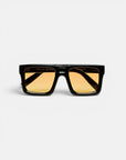 Eine schwarze, rechteckige Sonnenbrille von Okkia mit breitem Rahmen und gelb getönten Gläsern ist auf einem schlichten weißen Hintergrund zu sehen. Die Bügel der Sonnenbrille sind gekreuzt und unterstreichen das markante, moderne Design mit auffälligen Oversize-Proportionen, das für einen wahrhaft zeitgemäßen Look sorgt.