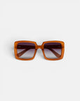Quadratische Sonnenbrille von Okkia mit einem breiten, glänzenden, bernsteinbraunen Kunststoffrahmen und dunklen Verlaufsgläsern, präsentiert vor einem schlichten weißen Hintergrund. Die sichtbaren Scharniere an den Bügeln und die Frontansicht unterstreichen das symmetrische Oversize-Design. Diese ISCHIA-Sonnenbrille von Okkia ist zudem mit polarisierten Gläsern ausgestattet, die für verbesserte Sichtklarheit und hohen Tragekomfort sorgen.