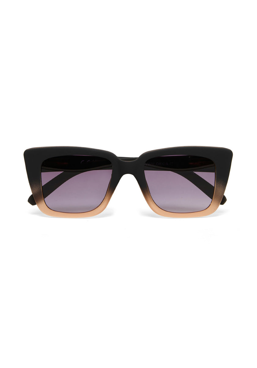 Okkia cat-eye sunglasses featuring thick black frames with a metallic gold accent along the bottom edge and dark gradient lenses that fade from deep tint at the top to lighter at the bottom, shown against a white background.
