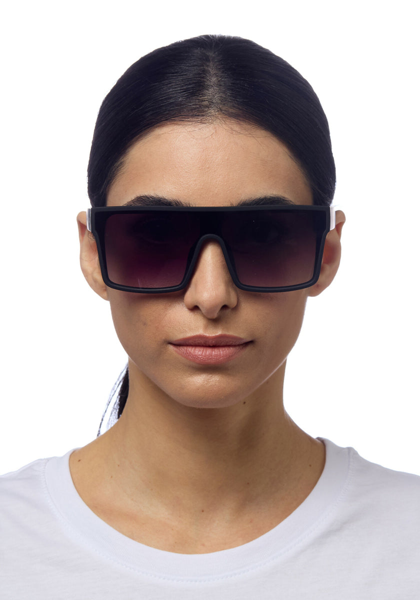 A woman with straight dark hair pulled back wears oversized, rectangular Okkia sunglasses with UV 400 protection and a plain white shirt. She faces forward against a white background, showing a neutral facial expression.