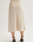 A person faces away, wearing a cream-colored Bella Dahl Lyocell midi skirt with a slight flare. The lightweight, silky skirt is styled with black strappy low-heeled sandals against a plain white background.