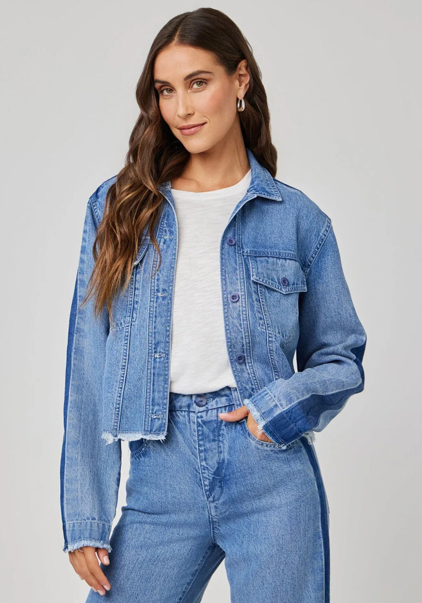 A woman with long brown hair wears a cropped Bella Dahl denim-look jacket over a white t-shirt and matching high-waisted jeans, standing confidently with one hand in her pocket against a plain light gray background.