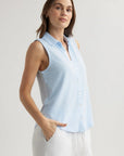 A woman with light skin and brown hair wears a sleeveless Bella Dahl Baumwollmix Top with Hemdkragen in light blue and white pants, standing confidently with one hand in her pocket against a plain light background.