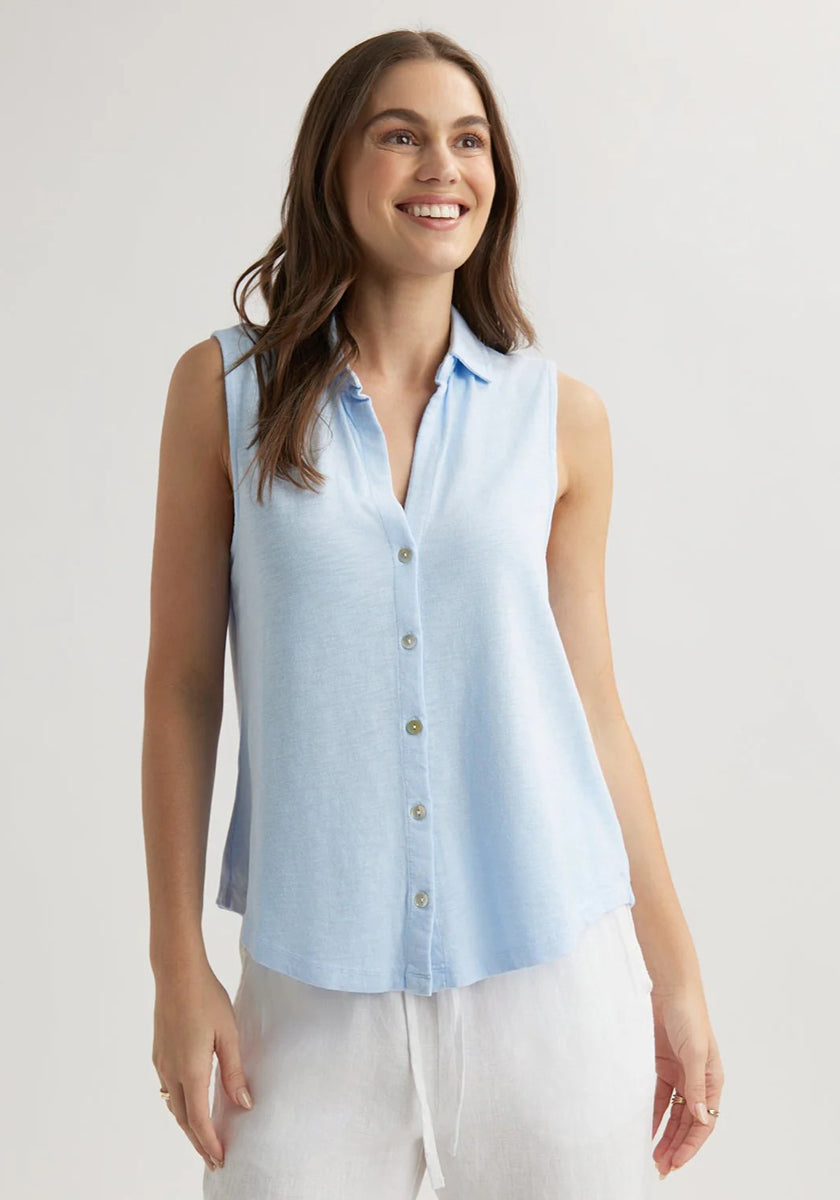 A woman with long brown hair smiles while wearing a sleeveless, light blue Bella Dahl Baumwollmix Top with Hemdkragen and loose white pants. She stands against a plain, light background with her arms relaxed by her sides.
