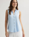 A woman with long brown hair smiles while wearing a sleeveless, light blue Bella Dahl Baumwollmix Top with Hemdkragen and loose white pants. She stands against a plain, light background with her arms relaxed by her sides.