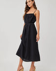 A woman poses sideways in a studio wearing a Bella Dahl Leinen Midikleid with verstellbaren Trägern and Bindegürtel, styled with gold hoop earrings and beige Keilsandalen. She has long brown hair and stands against a plain background.